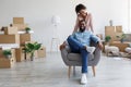 Glad smiling young afro american husband sitting in armchair, wife standing near him in apartment with cardboard boxes Royalty Free Stock Photo