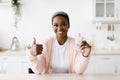Glad smiling young pretty black woman with perfect skin holds glass with clean water and shows thumb up Royalty Free Stock Photo