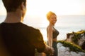 Glad young african american female in sportswear leads male by hand in morning on rocks near ocean