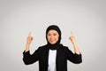 Glad young asian woman in suit, hijab point fingers up at empty space