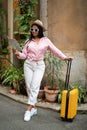 Glad young black lady in casual sunglasses with suitcase looking at map, enjoy trip in new city, outside, vertical