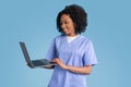 Glad young black lady doctor nurse in blue uniform uses laptop for video call Royalty Free Stock Photo