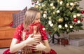 Glad young woman sitting and embracing gift boxes near xmas fir tree. Happy alone woman with pile of presents