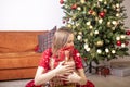 Glad young woman sitting and embracing gift boxes near xmas fir tree. Happy alone woman with pile of presents