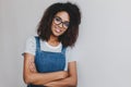 Glad young woman wears denim clothes and trendy glasses posing with gently smile. Attractive curly girl with bronze skin