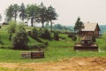 A glade with a pond, bushes and wooden buildings in the style of the wartime of the USSR of the Second World War