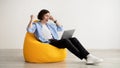 Gladful guy using laptop and raising hands in joy, celebrating success, sitting in beanbag chair, panorama