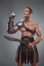 Gladiator in armour posing with sword over grey Royalty Free Stock Photo