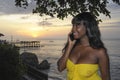 glamorous African American black woman in chic and elegant summer dress talking on mobile phone at sunset beach