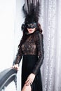 Glamorous brunette lady with a beautiful hairstyle and red lips, in an evening dress, a Venetian black mask with stylish accessori