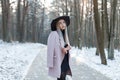 Glamorous cute beautiful young woman in stylish warm glamorous clothes in an elegant hat is stands on the road in a snowy park Royalty Free Stock Photo