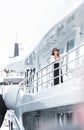 A glamorous diva in an evening dress of black color and sunglasses stands on the top deck of a huge yacht in