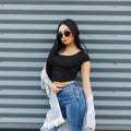 Glamorous elegant young hipster woman in black sunglasses with long hair in a black trendy t-shirt in a summer jacket Royalty Free Stock Photo