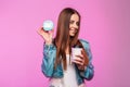 Glamorous funny young woman in stylish denim jacket with cup of tea or coffee posing with donut in mask near the glamorous pink Royalty Free Stock Photo