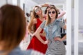 Glamorous girls trying on sunglasses posing in front of the mirror in fashion boutique