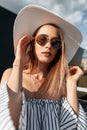 Glamorous gorgeous pretty young woman in fashion sunglasses in straw hat in striped dress straightens hair. Sunny portrait Royalty Free Stock Photo