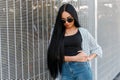 Glamorous pretty urban hipster woman in stylish summer jacket in black sunglasses in a black t-shirt in high waist jeans Royalty Free Stock Photo