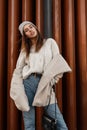 Glamorous stylish model of a young woman in a trendy hat in a knitted fashion sweater in an elegant fur coat of milk color in Royalty Free Stock Photo