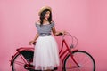 Glamorous tanned girl in long skirt standing near red bicycle. Enchanting young woman in straw hat Royalty Free Stock Photo