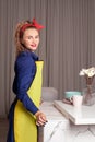 Glamorous woman in blue and yellow dress standing in the kitchen. Pinup housewife with trendy makeup