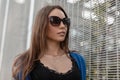 Glamorous young pretty hipster woman in a knitted blue cape in fashionable sunglasses in a black t-shirt is standing Royalty Free Stock Photo