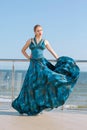 A glamorous young woman in a dark blue dress. The serious girl on a glass balcony. The female on a bright blue sky background.