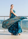 A glamorous young woman in a dark blue dress. A serious girl on a glass balcony. A pretty female on a bright blue sky background.