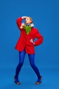 Glamorous young woman with makeup. Weird girl with flowers in unusual, strange, red jacket posing against blue color Royalty Free Stock Photo