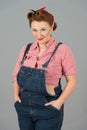 Glamour brunette female in american worker style with pin-up makeup. Woman in denim and red shirt in studio on gray