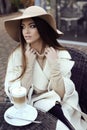 Glamour girl with dark straight hair wears luxurious beige coat with elegant hat