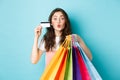 Glamour girl showing plastic credit card and shopping bags, pucker lips for kiss, standing happy against blue background Royalty Free Stock Photo