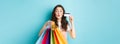 Glamour girl showing plastic credit card and shopping bags, pucker lips for kiss, standing happy against blue background Royalty Free Stock Photo