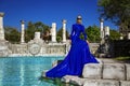 Glamour, stylish elegant woman in blue long evening gown dress is posing near the pool in luxury resort outdoor Royalty Free Stock Photo