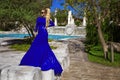 Glamour, stylish elegant woman in blue long evening gown dress is posing near the pool in luxury resort outdoor Royalty Free Stock Photo