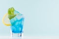 Glamour tropical fruit blue cocktail with curacao, ice cubes, green mint, lemon slice in misted shot glass in modern mint color. Royalty Free Stock Photo