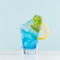 Glamour tropical fruit blue cocktail with curacao, ice cubes, sugar rim, green mint, lemon in misted shot glass in modern mint. Royalty Free Stock Photo