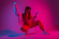 Glamour young woman dancer in fashionable youth clothes in a white sneakers sits in a room with bright pink light. Modern girl Royalty Free Stock Photo