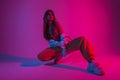 Glamour young woman dancer in fashionable youth clothes in a white sneakers sits in a room with bright pink light. Sexy modern Royalty Free Stock Photo