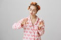 Glamourous girl at home wearing hair curlers and lovely pajamas in hearts, blowing at fingers while painting nails Royalty Free Stock Photo