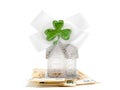 Glamourous home with glitter and white bow with green shamrock on stack of cash on white background. Buying high value house
