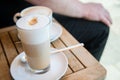 Glas of Latte Macchiato and cup of Cappuccino coffee with milk on wooden table outside of street caf