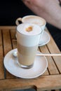 Glas of Latte Macchiato and cup of Cappuccino coffee with milk on wooden table outside of street caf