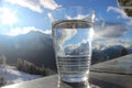 Glas of mineral water on railing with mountain landscape and blue cloudy sky Royalty Free Stock Photo