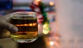 a glass of alcohol whisky held in hand with background blur bokeh lights