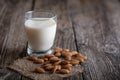 A glass with almond vegetable milk stands on a wooden table. Almond nuts are next to the glass