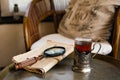 A glass in an antique cup holder with tea and old newspaper with a loupe are on a copper table Royalty Free Stock Photo