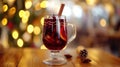 A glass of aromatic red hot mulled wine with cinnamon, orange and muscat stands on wooden table with lamps and christmas