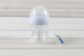 Glass baby bottle and baby pacifier on white wooden background