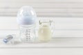 Glass baby bottle, milk jug and baby pacifier on white wooden ba