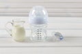 Glass baby bottle, milk jug and baby pacifier on white wooden ba